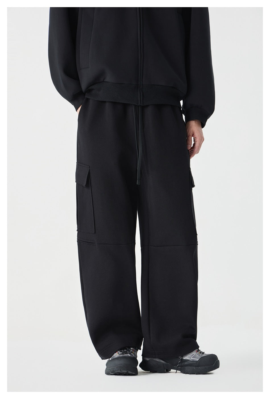 Cropped front view of a model wearing black wide-leg cargo pants with large flap pockets and a drawstring waist.