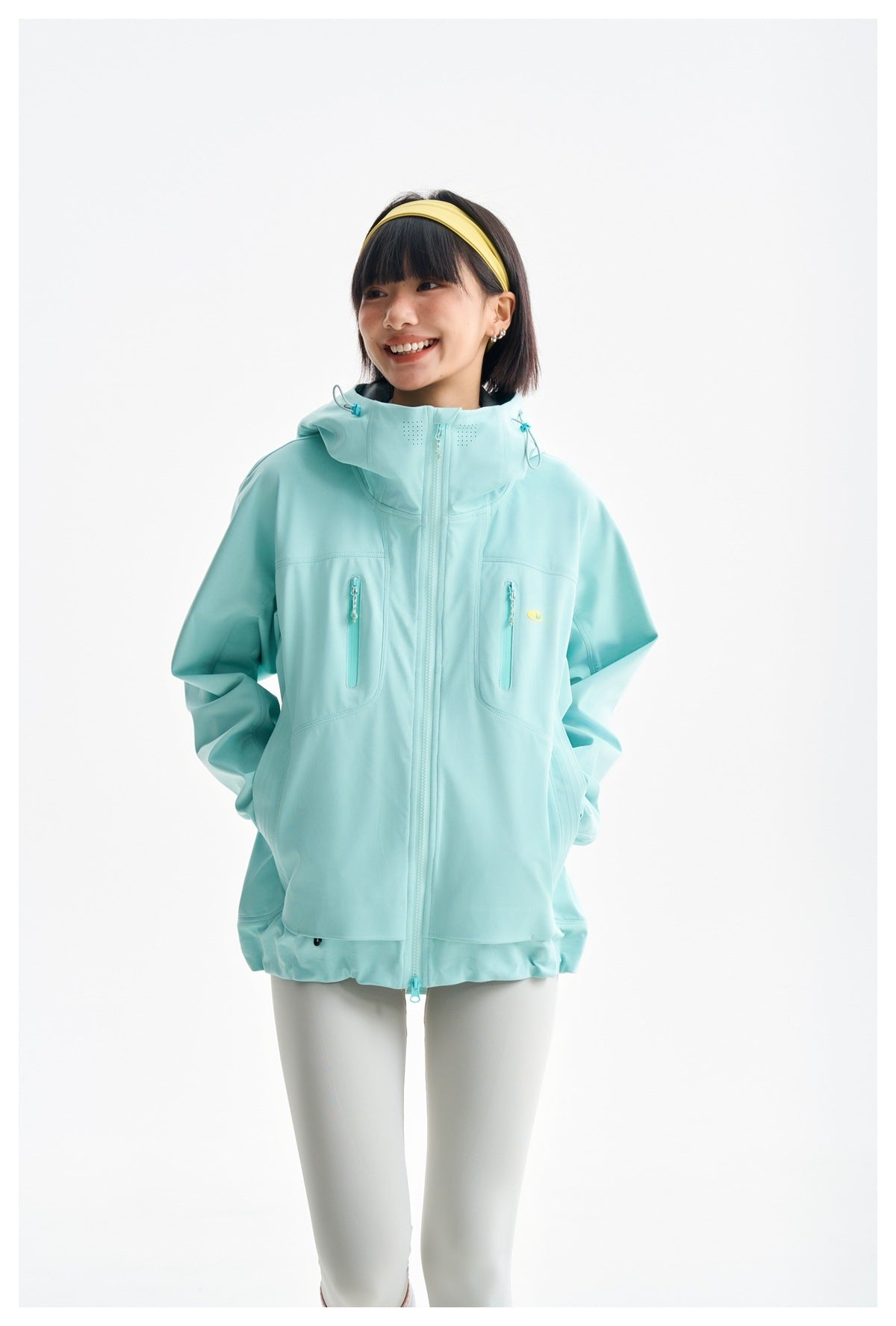 Model wearing an aqua hooded jacket with hands in its side pockets, shown from the front.