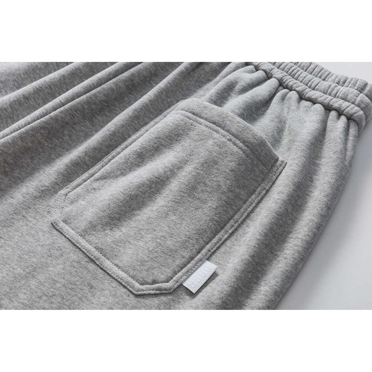 Close-up of gray sweatpants with a large front pocket and a small white fabric tab.
