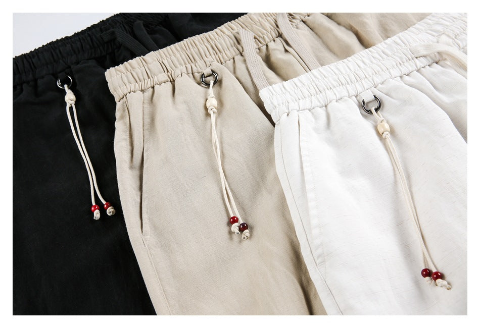 Close view of black, beige, and white pants with elastic waistbands, metal drawstring loops, and beaded cord ends.