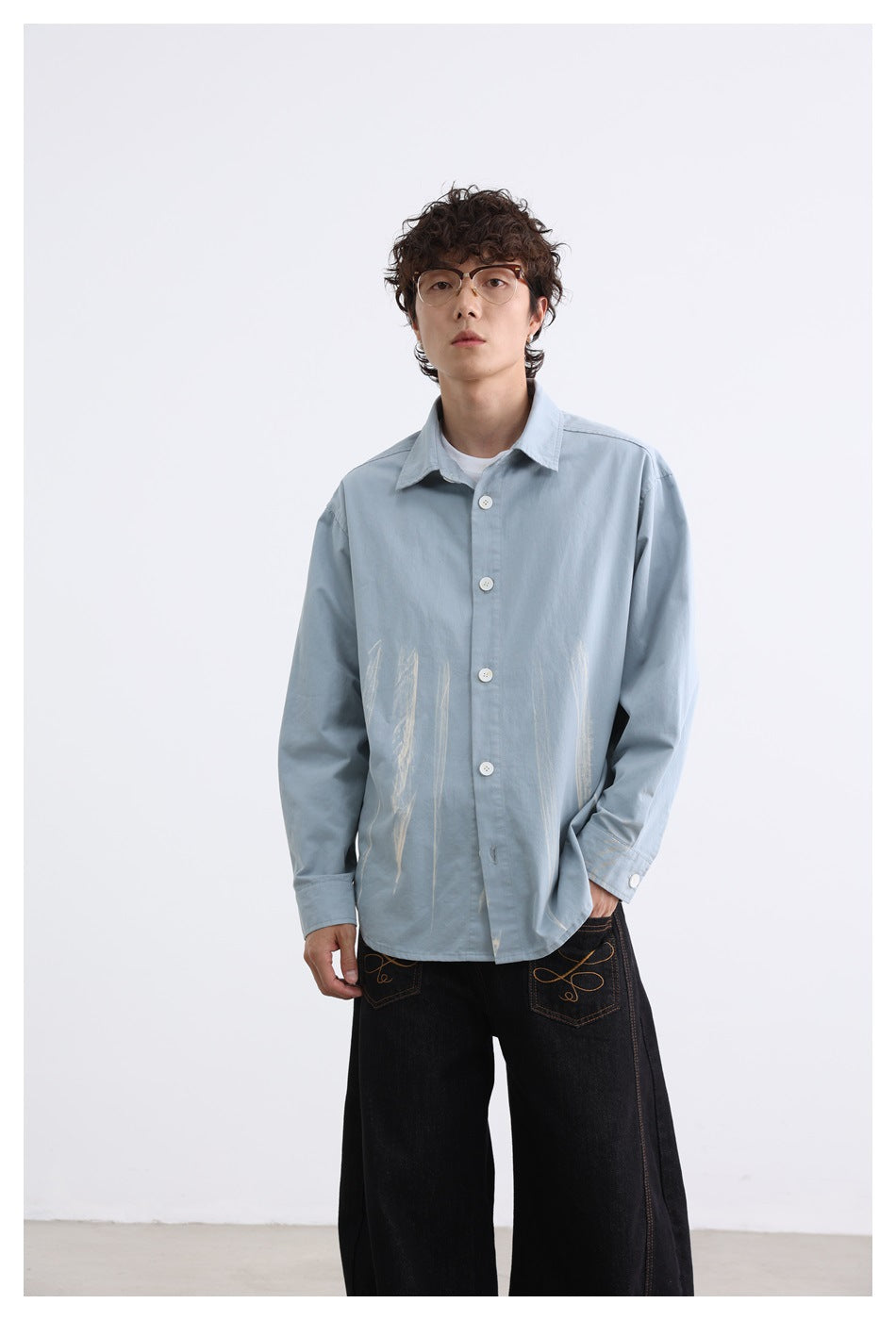 Model wearing the blue button-up shirt with cream brushstroke marks, front view with black wide-leg jeans