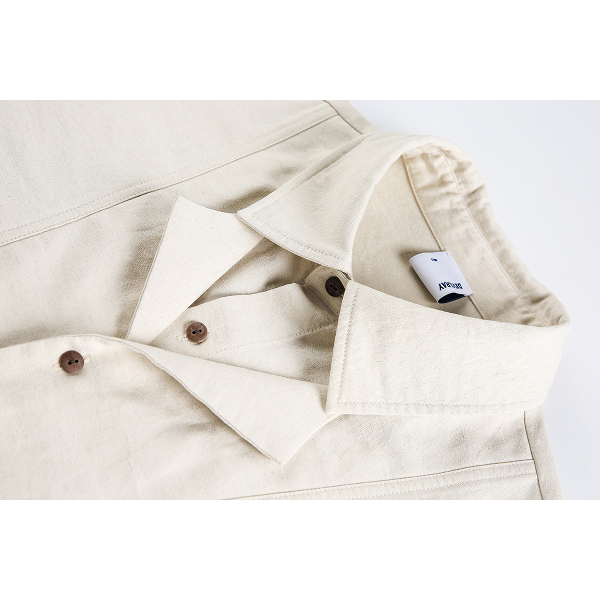 Close-up of an ivory shirt collar, brown buttons, stitching, and a small white neck label.