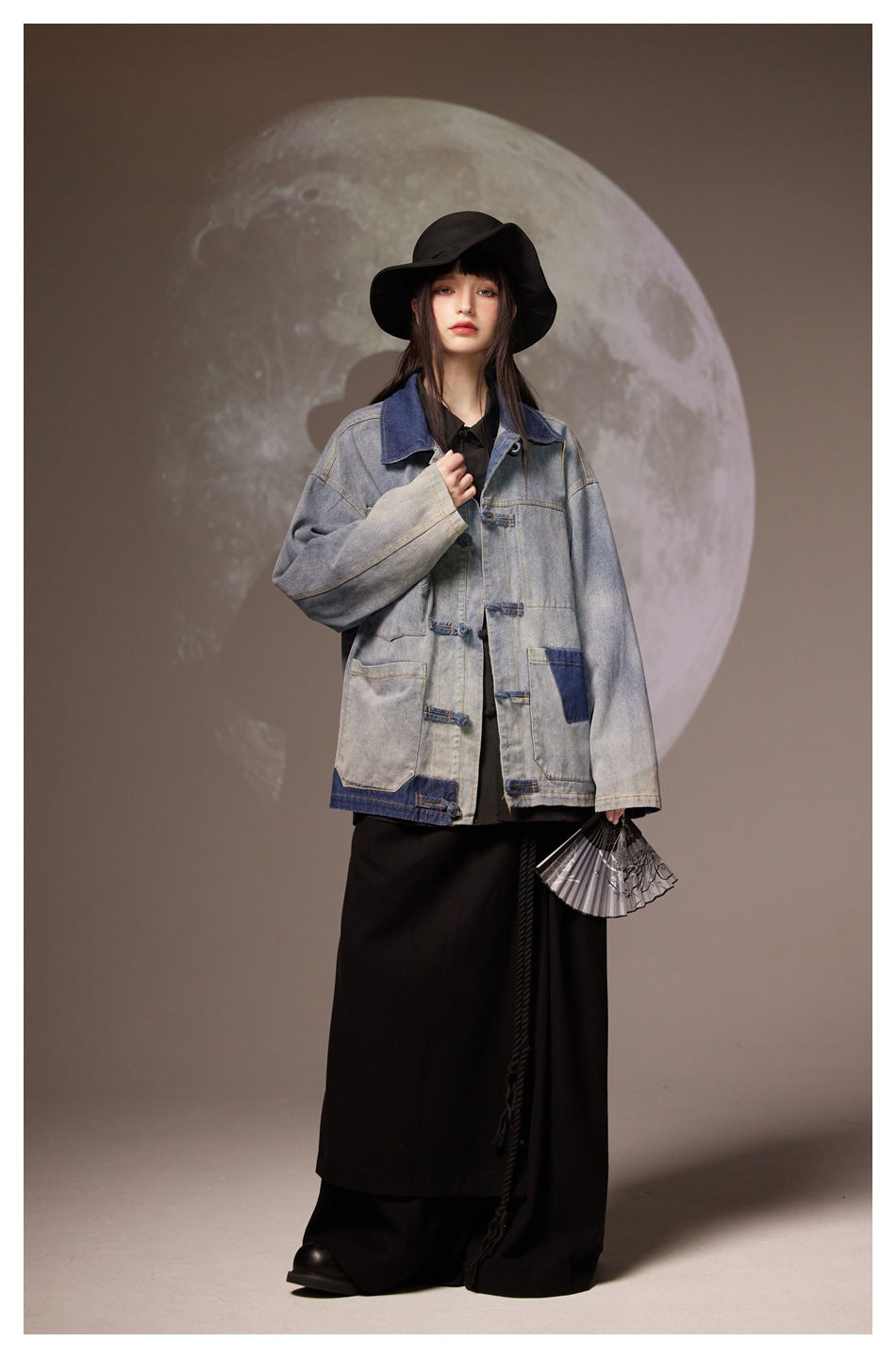 Full-length view of a model wearing a gray denim jacket with dark blue accents over a long black outfit.