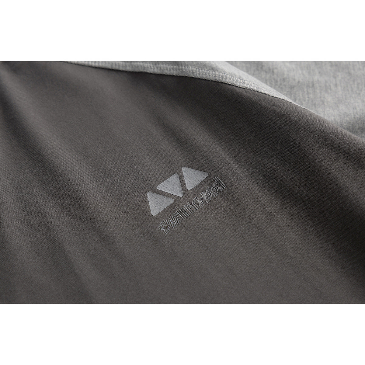 Close-up of a small raised geometric logo on the charcoal fabric of a T-shirt.