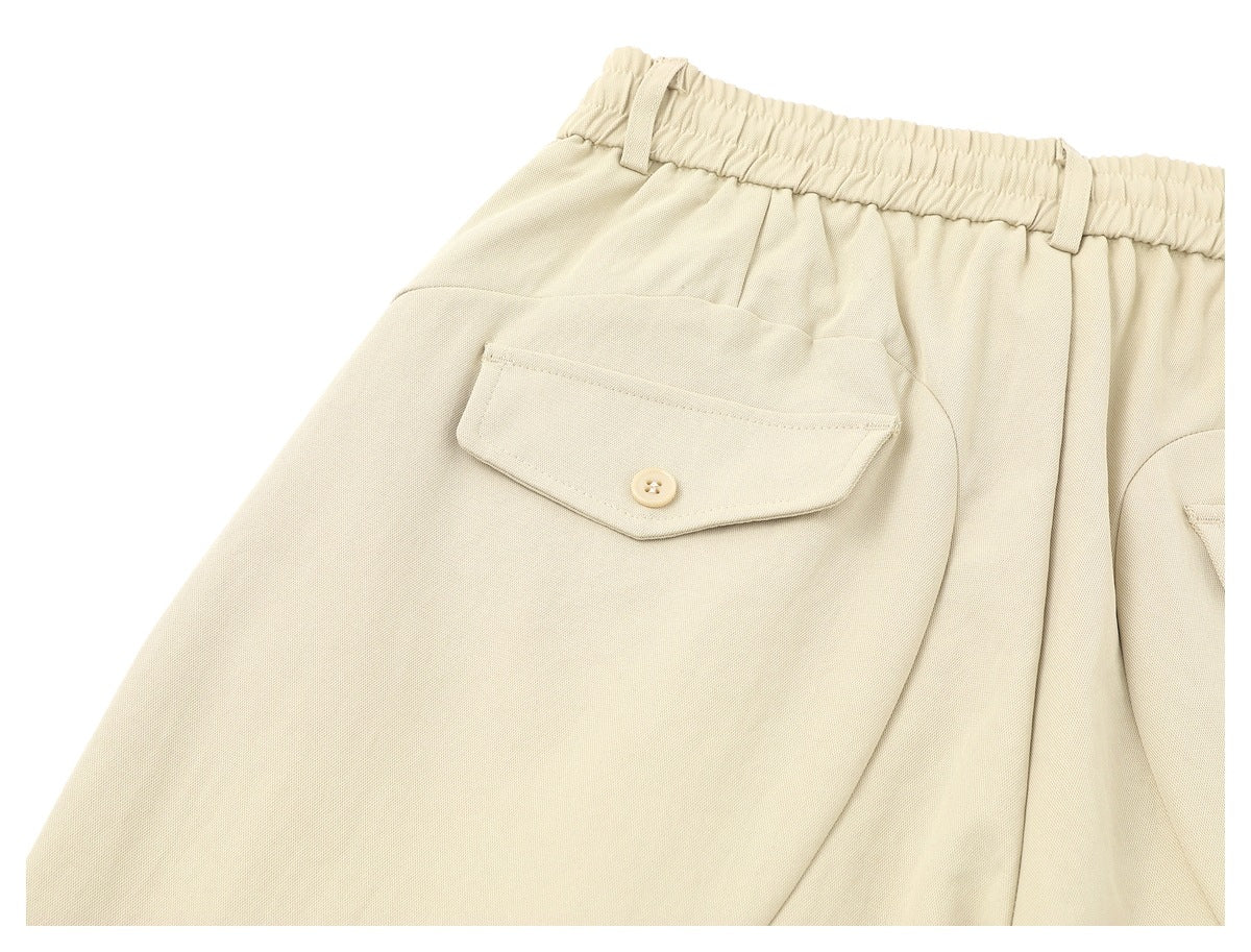 Close-up of cream trousers showing an elastic waistband, belt loops, and a buttoned flap back pocket.