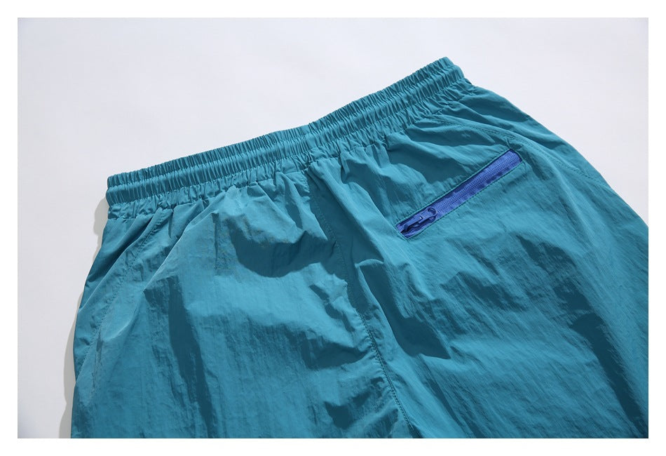 Flat lay of teal shorts showing the elastic waistband and a blue zippered pocket.