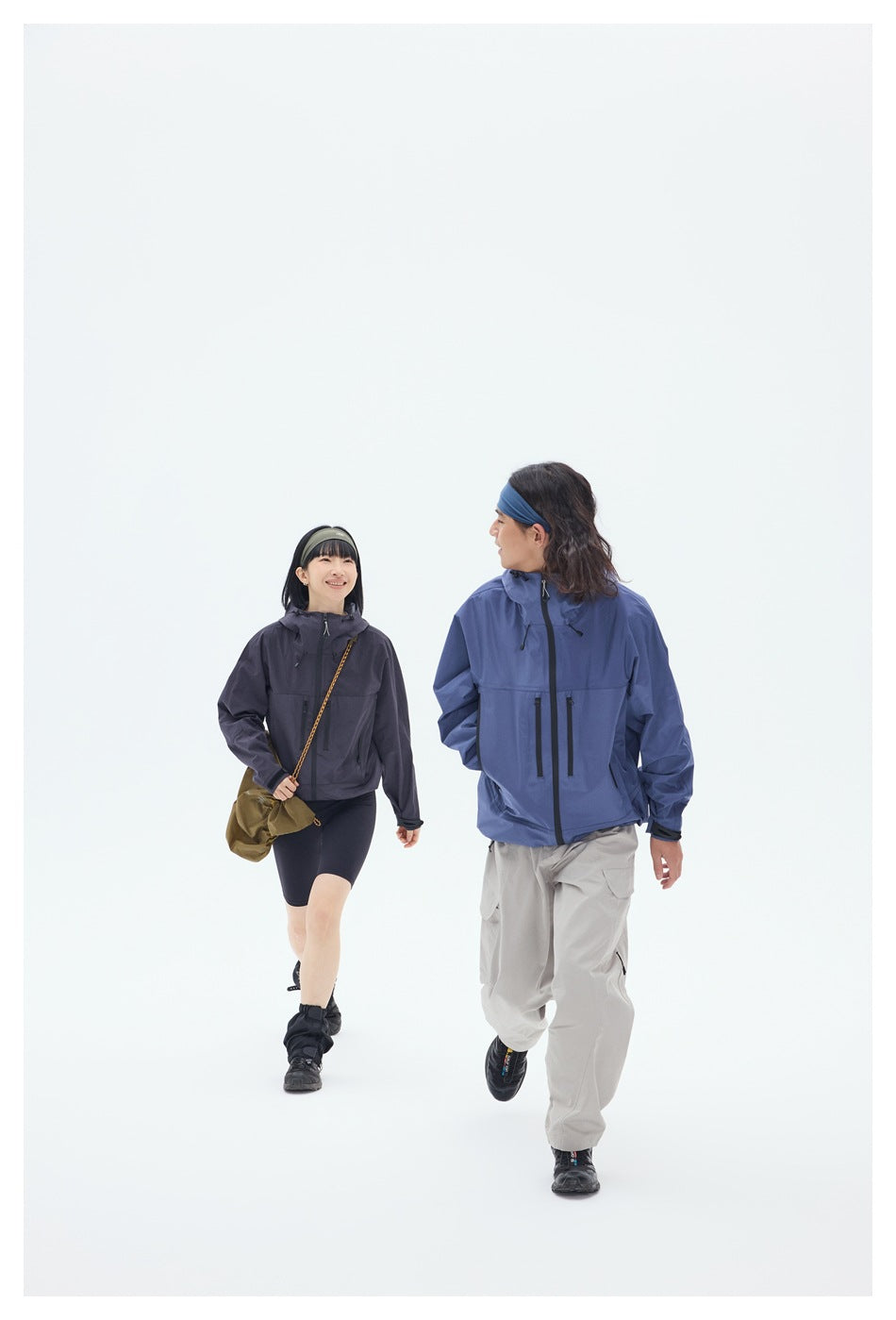 Two models walk toward the camera in charcoal and blue hooded jackets; the blue jacket is shown from the front.