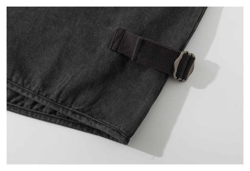 Close-up of a charcoal garment hem with an adjustable woven strap and metal buckle.