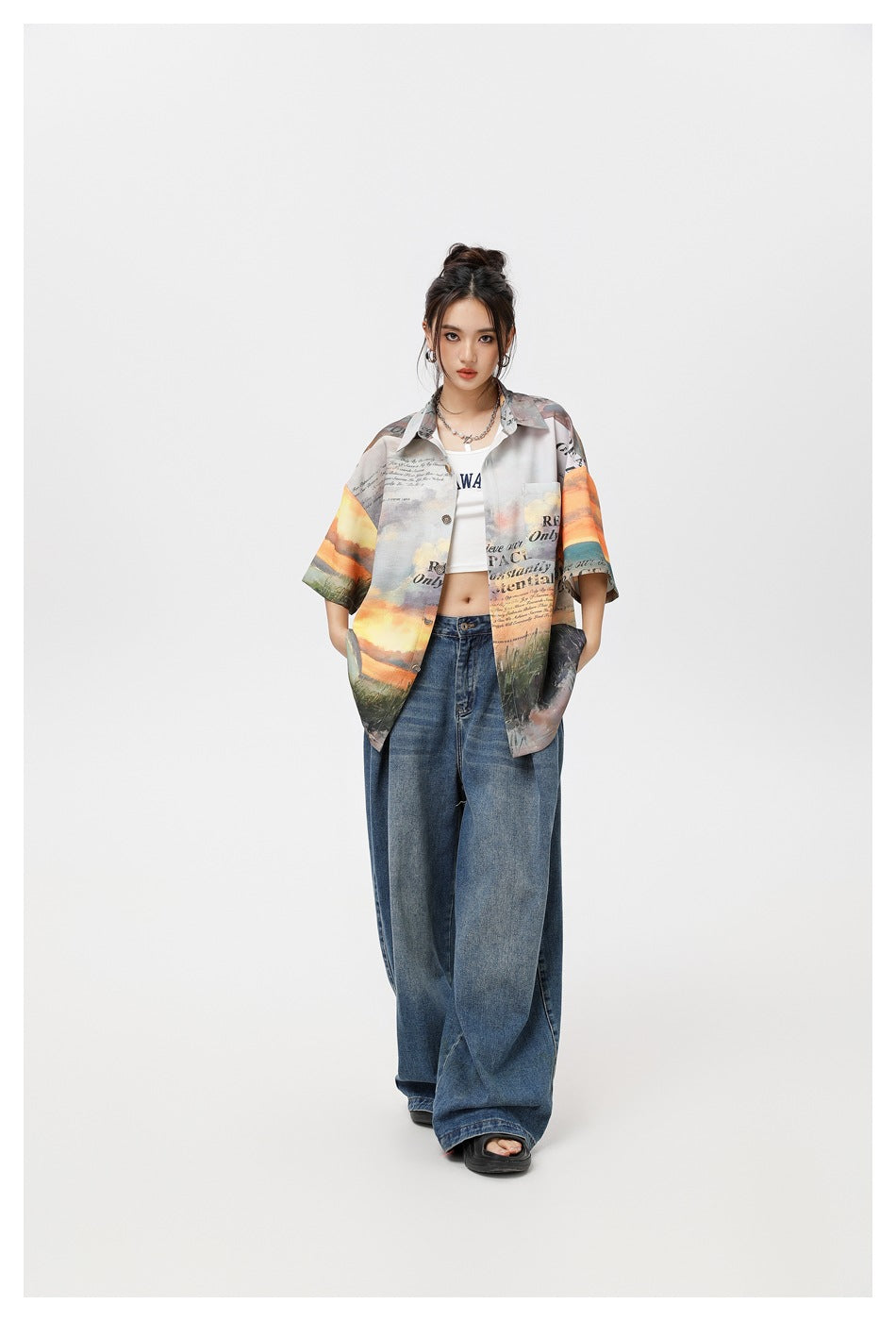 Full-length front view of a model wearing an oversized multicolored printed shirt with wide-leg blue jeans.