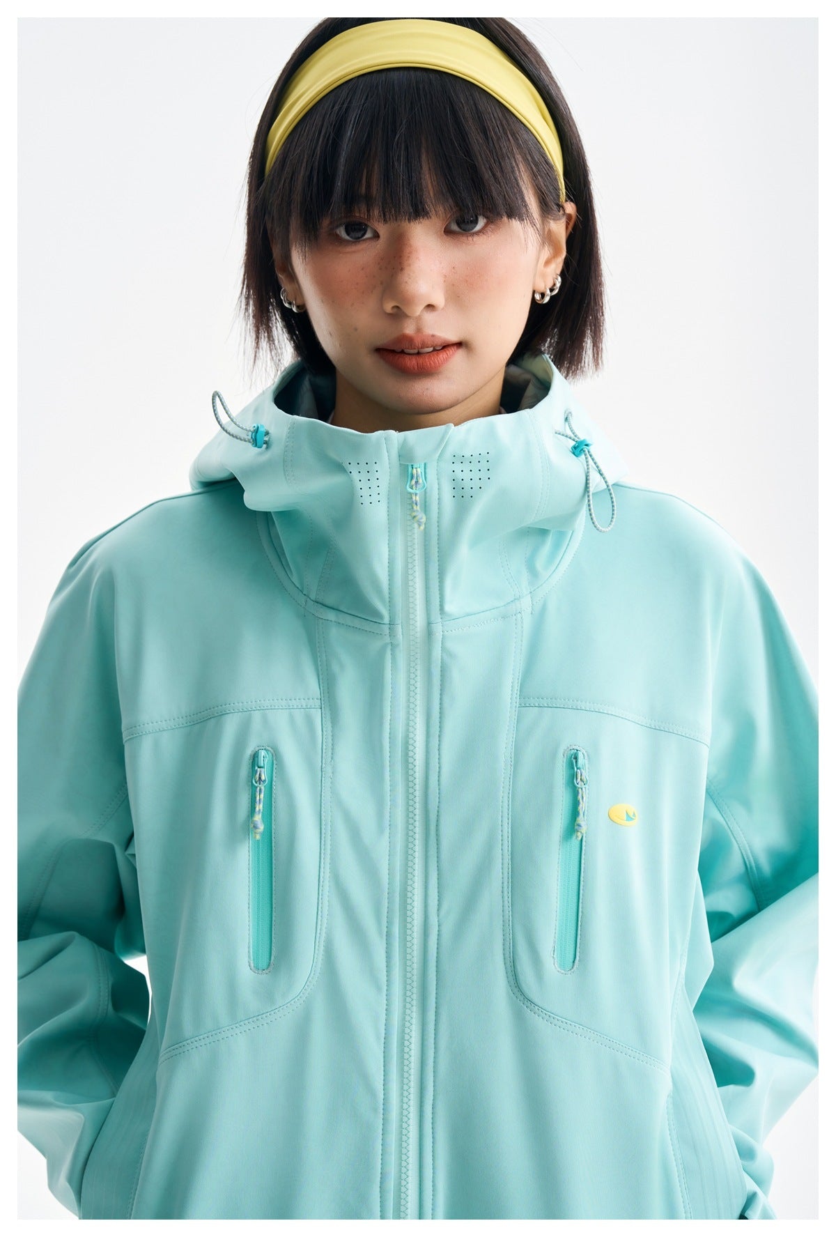 Close front view of an aqua jacket showing its high hood, center zipper, and two vertical zip pockets.