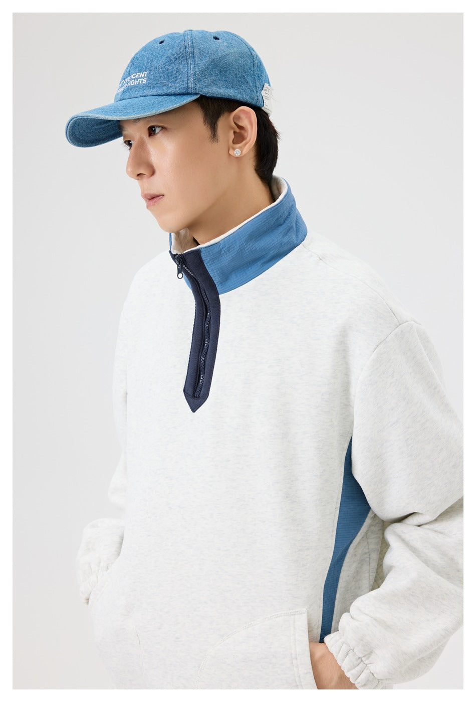 Close view of a man wearing a light gray pullover with a blue stand collar, navy quarter zip, and blue side panel.