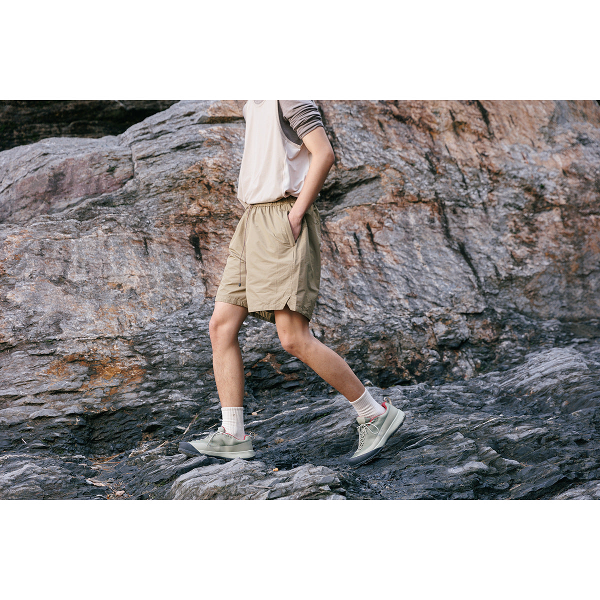Cropped model walking on rocks in khaki elastic-waist shorts with pockets and a white top.