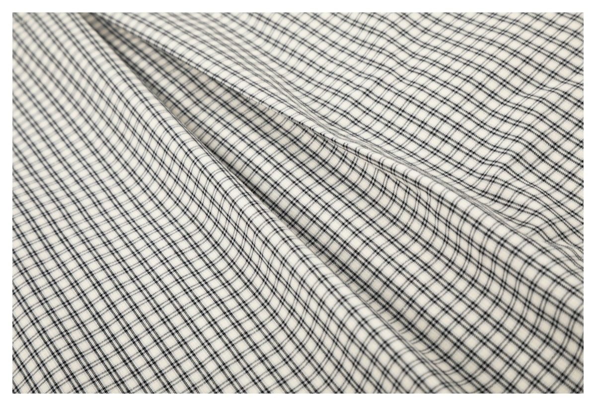 Close-up of the cream shirt's black plaid fabric, folded to show its pattern and stitching.