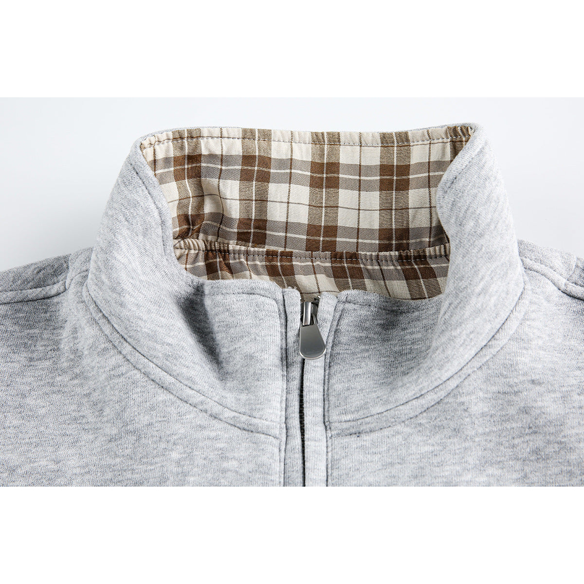 Close-up of a light gray zip-up jacket collar with brown plaid lining and a metal zipper pull.
