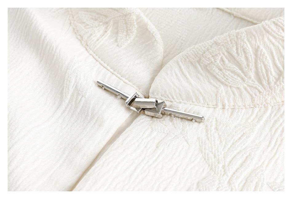Close-up of a silver metal clasp fastening the floral-textured ivory shirt fabric.