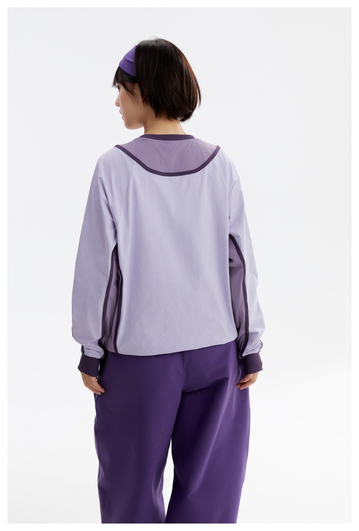 Back view of a model wearing a light lavender long-sleeve top with dark purple trim and purple trousers.