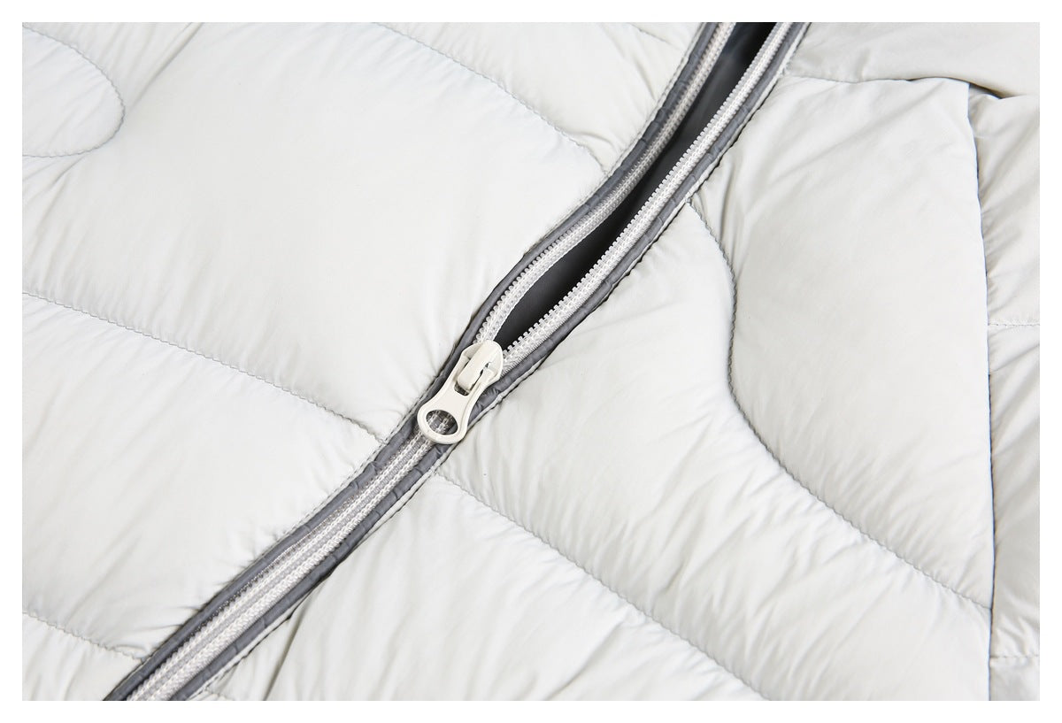 Close-up of a light gray puffer jacket's front zipper and pull against quilted panels.