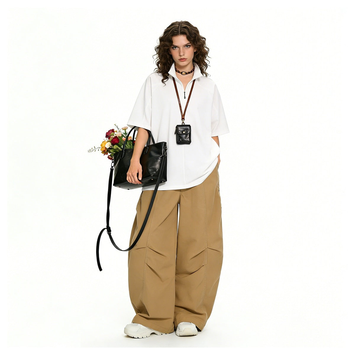 Model wearing khaki wide-leg pants with a white short-sleeve zip top, carrying a black bag with flowers