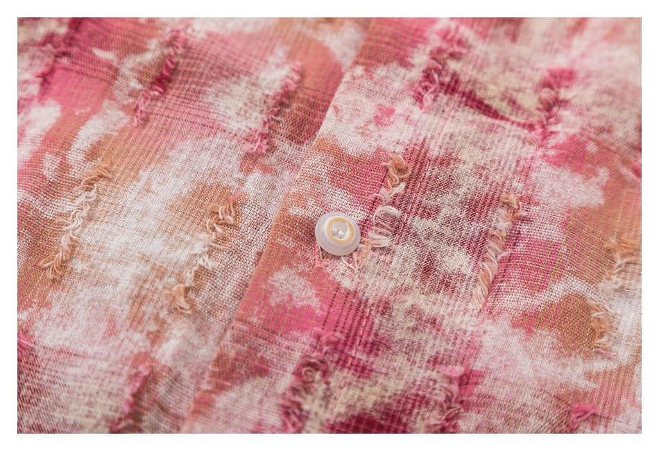 Close-up of a button and frayed woven texture on pink, cream and tan plaid fabric.