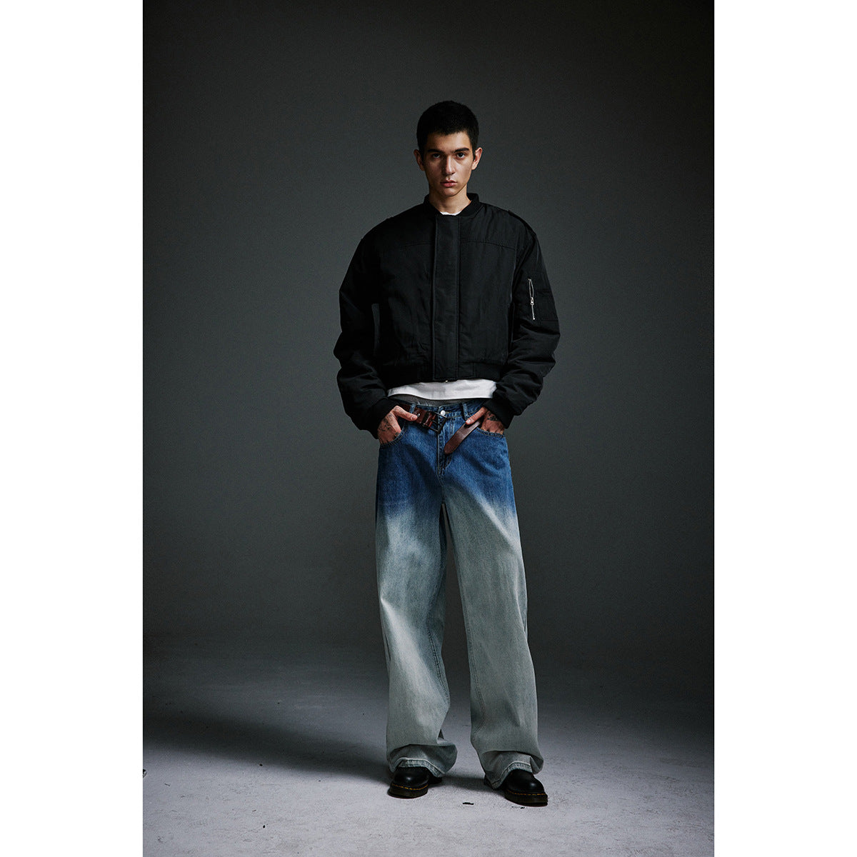 Front view of a model wearing a black bomber jacket and very wide blue jeans with pale washed legs.