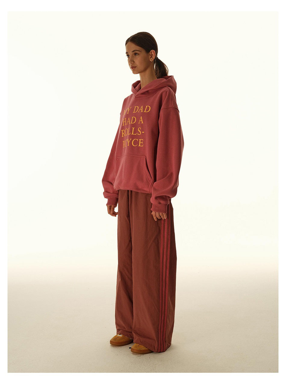 Model in a rose hoodie with yellow text and matching loose track pants with side stripes, shown in profile.