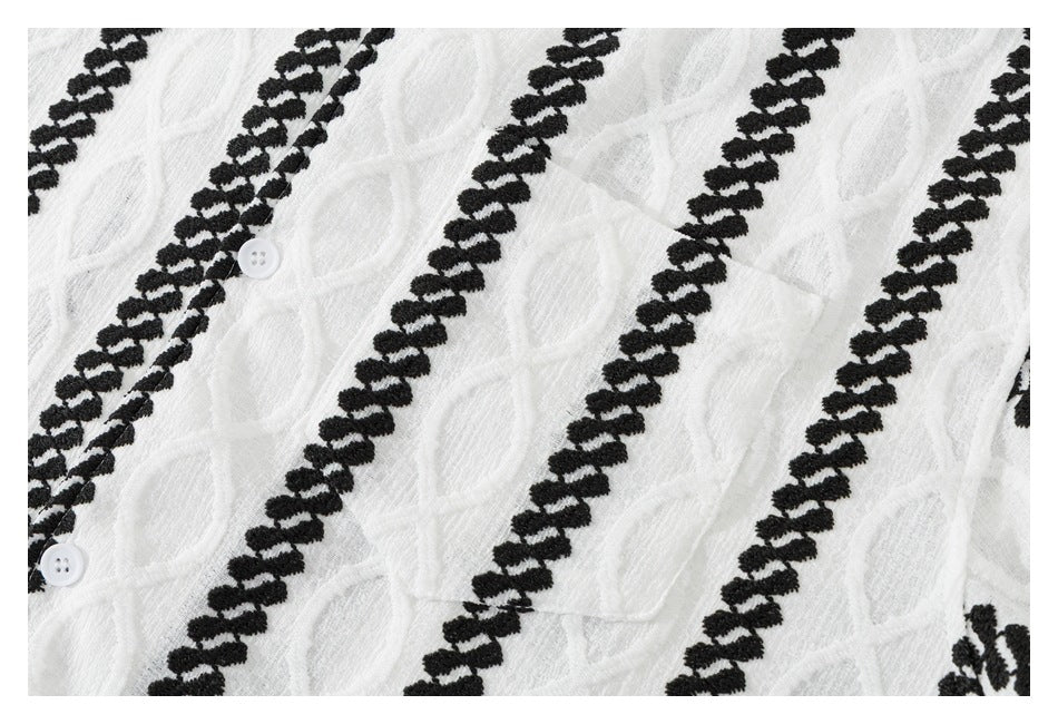 Close-up of white textured garment fabric with diagonal black embroidered bands and two white buttons.