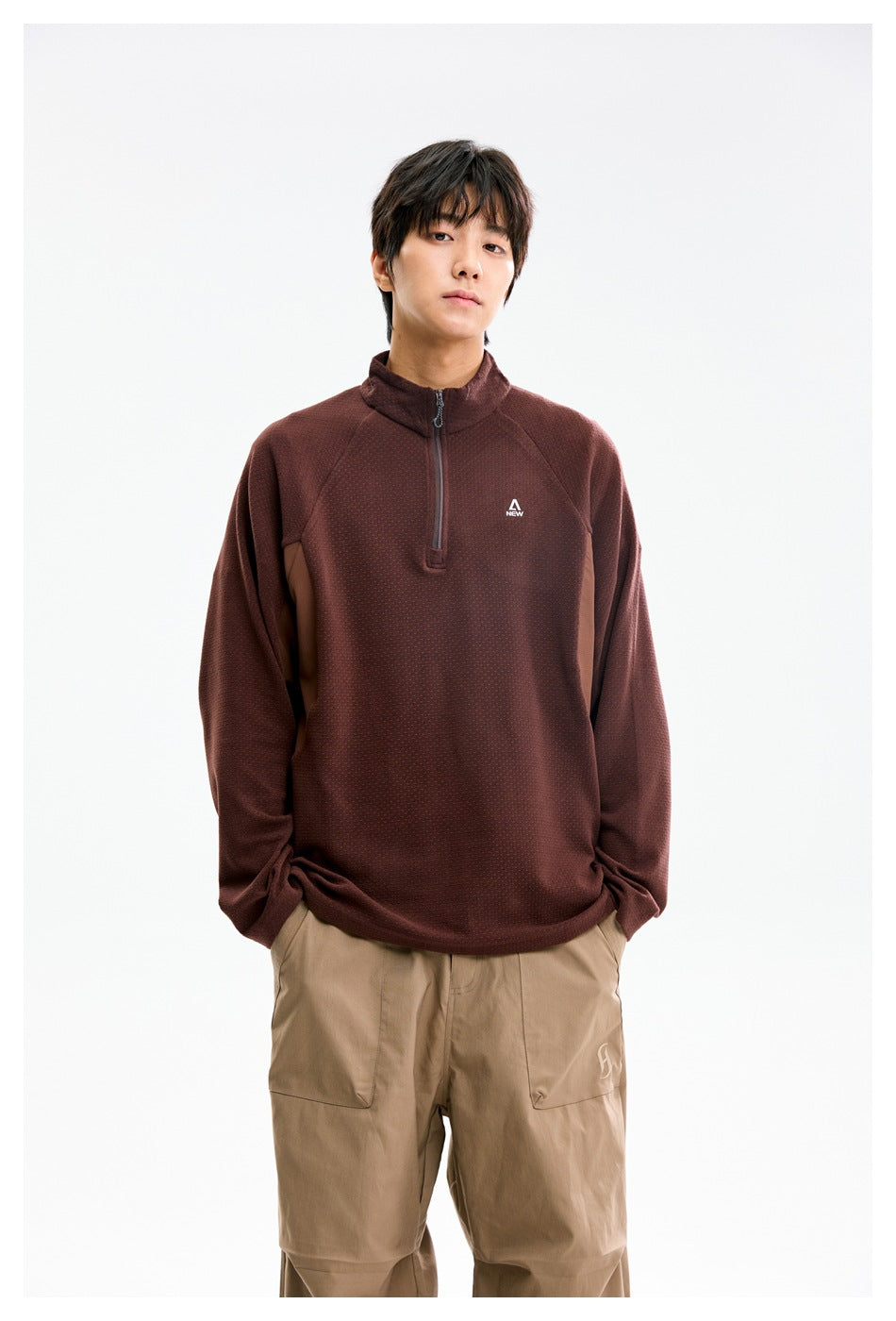 Model wearing a burgundy quarter-zip pullover with a stand collar and tan trousers, front view.