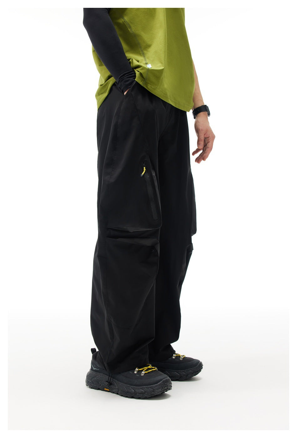 Model wearing black wide-leg cargo pants with zippered thigh pocket and flap pocket, green top and black sneakers, side view