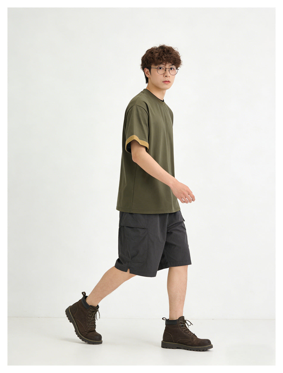 Side view of a model wearing an olive T-shirt with mustard sleeve cuffs and charcoal shorts.