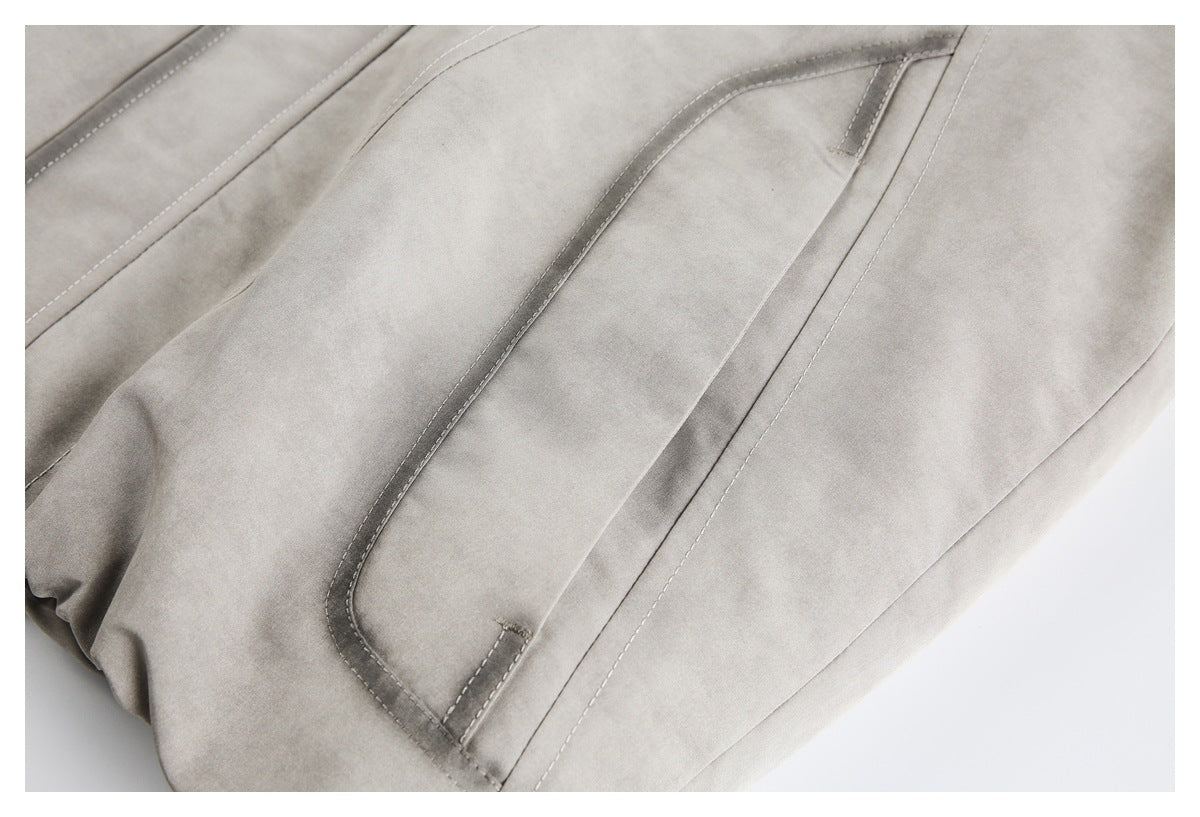 Close-up of a light gray jacket's curved, bound pocket opening and surrounding seams.