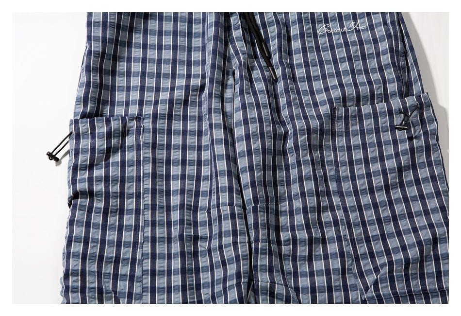 Close-up of blue and gray plaid pants showing large pockets, black cord toggles, and white embroidered lettering.