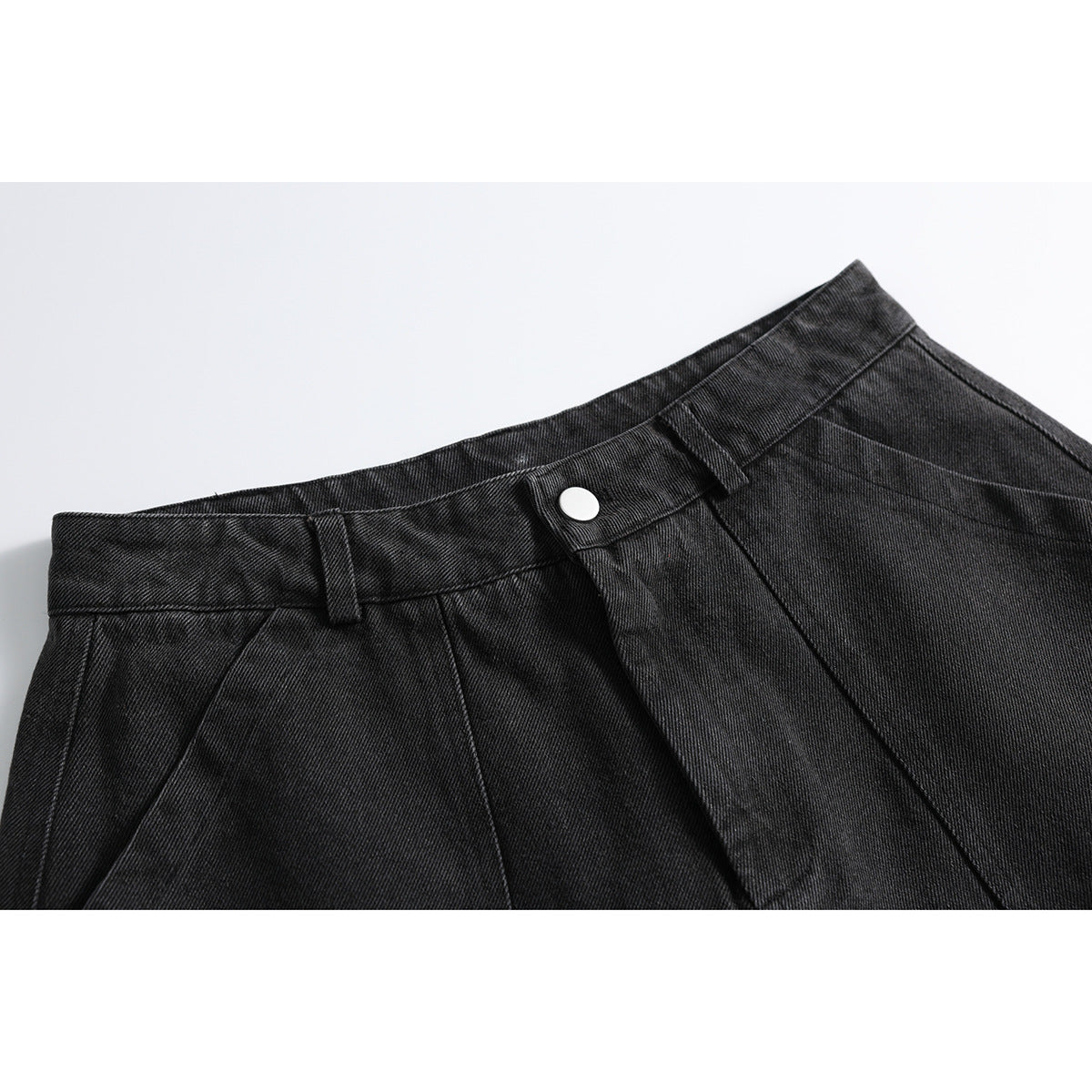 Close-up of charcoal-black denim trousers showing the waistband, belt loops, silver button and front pleats.