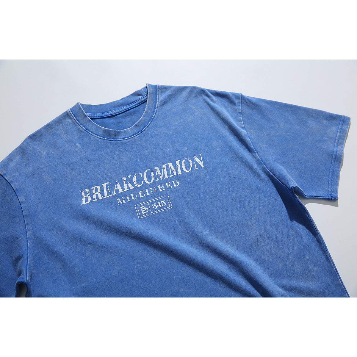 Flat lay of a blue short-sleeve crew-neck T-shirt with distressed white chest lettering and a boxed emblem.