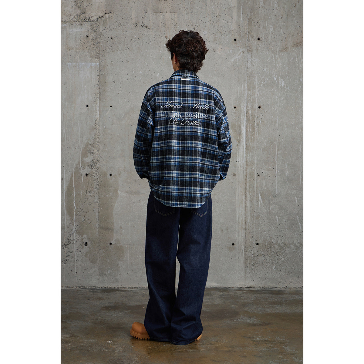 Back view of a model in a blue-and-black plaid shirt with embroidered English text across the upper back.