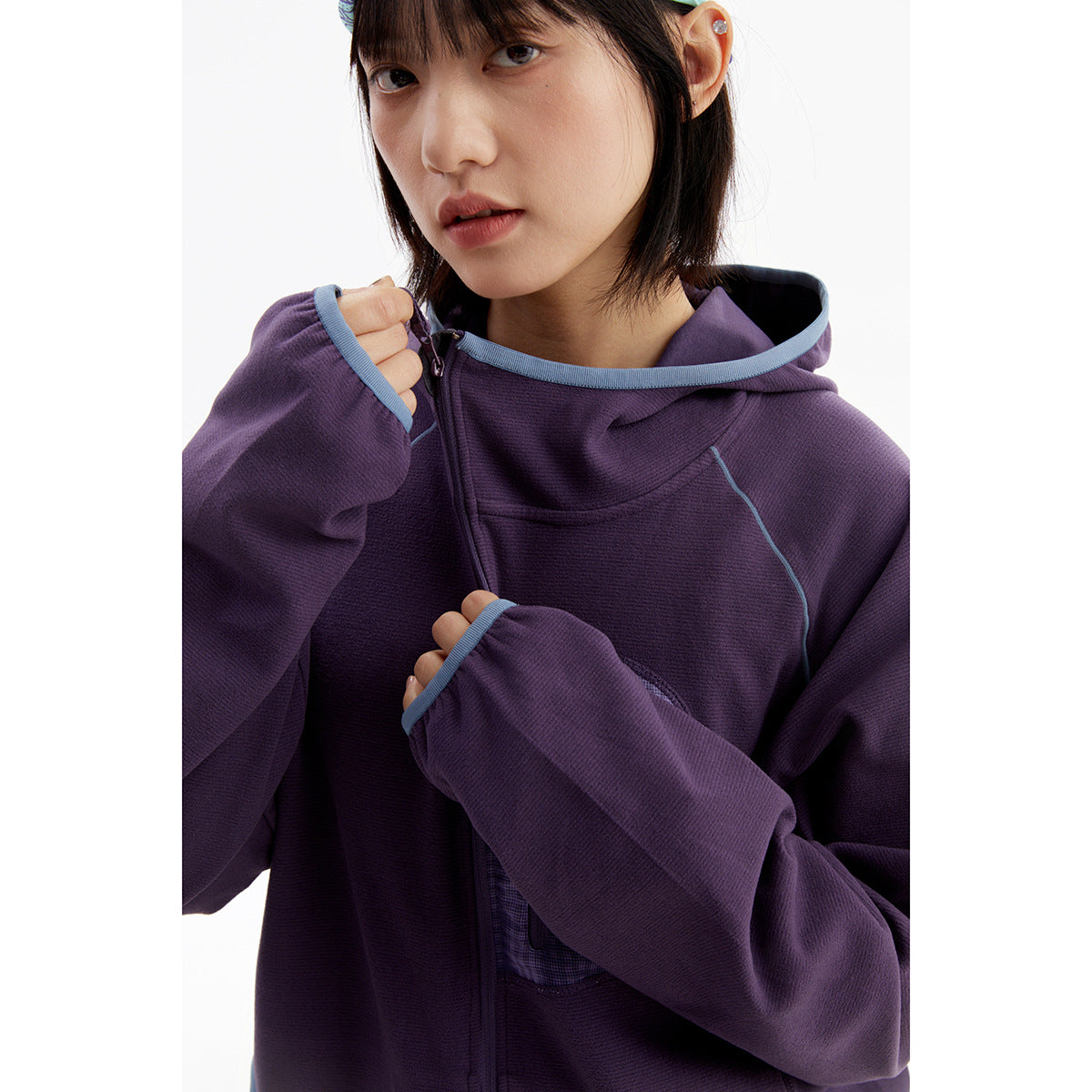 Close-up of a model wearing a purple zip-up hoodie with blue trim, a hood, and a plaid chest pocket.