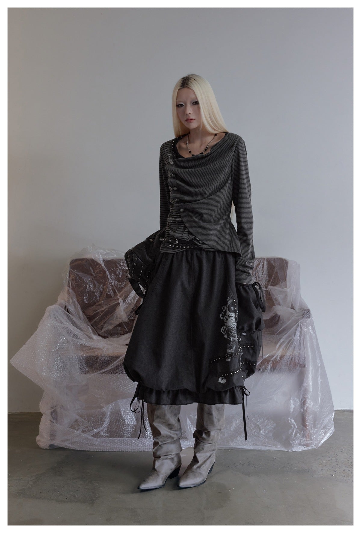 Model in the gray striped draped top with ruched front and asymmetric hem, styled with a dark skirt and gray boots