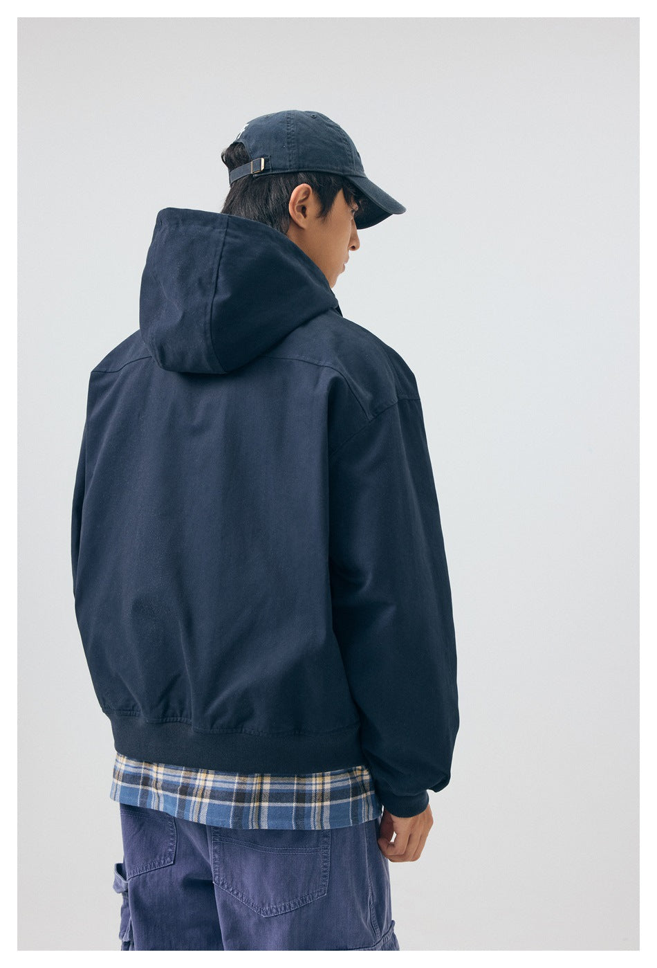 Rear three-quarter view of a model wearing the navy hooded jacket, showing its plain back and hood.
