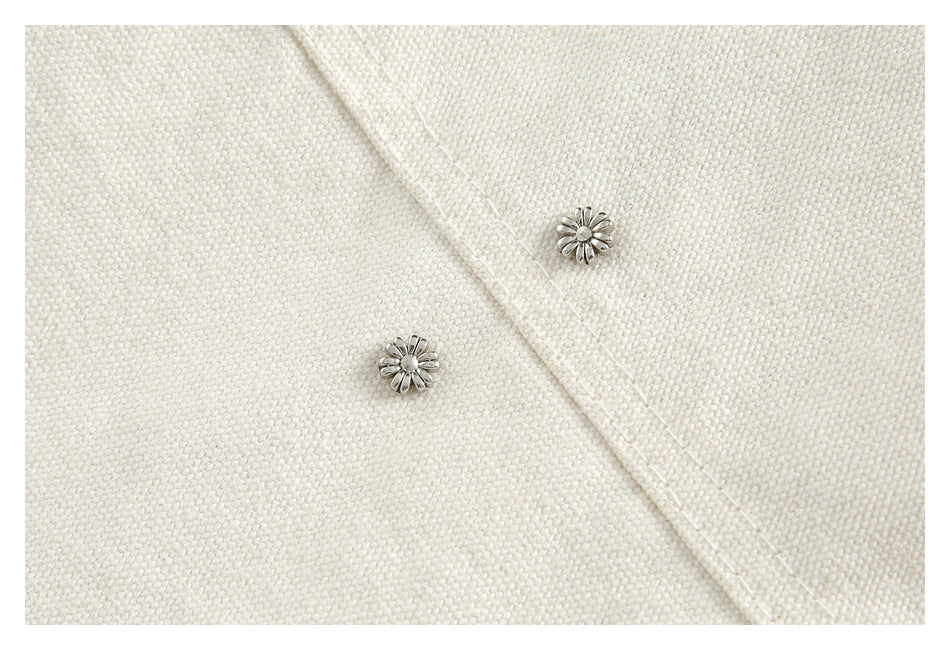 Close-up of two silver floral buttons on the textured ivory fabric of a garment.