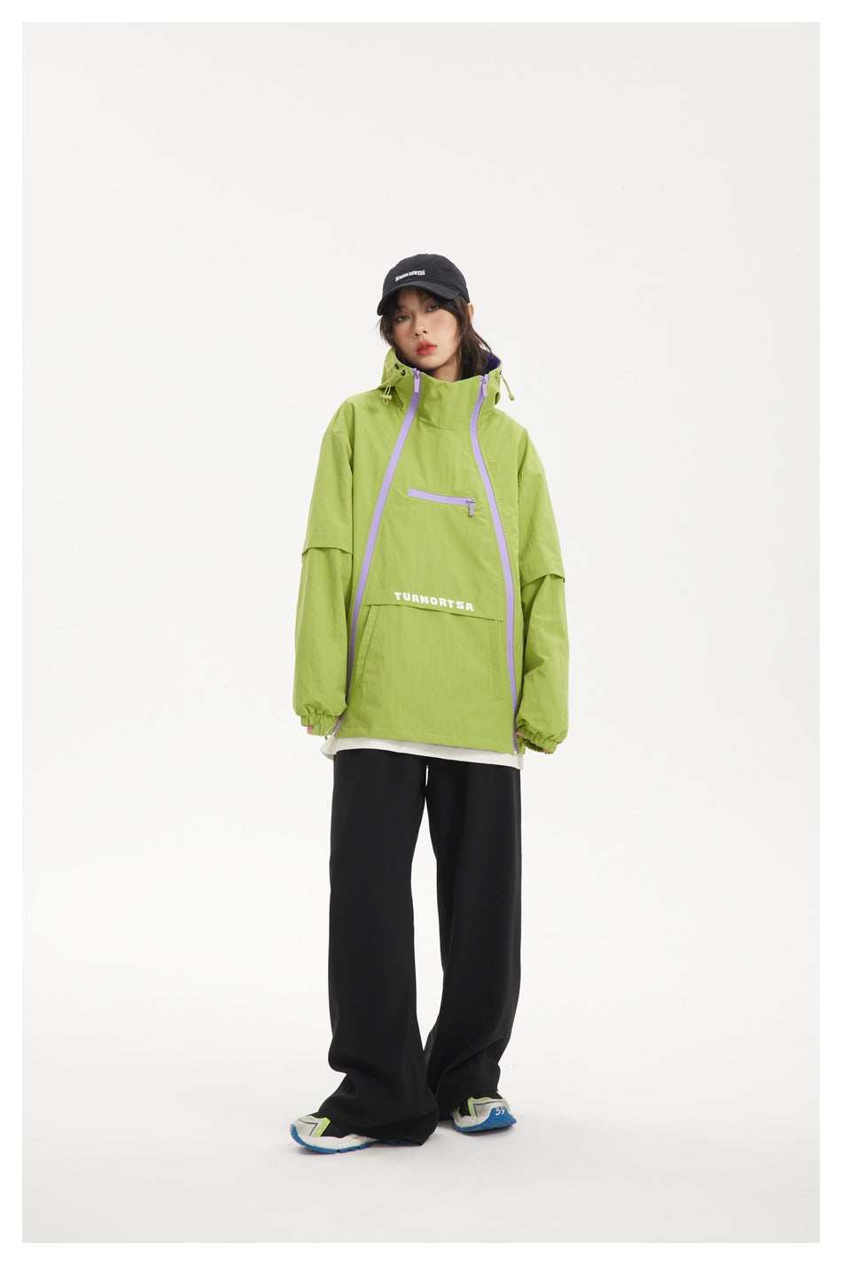 Model wearing lime green hooded jacket with lilac diagonal zippers over a white layer and black wide-leg pants