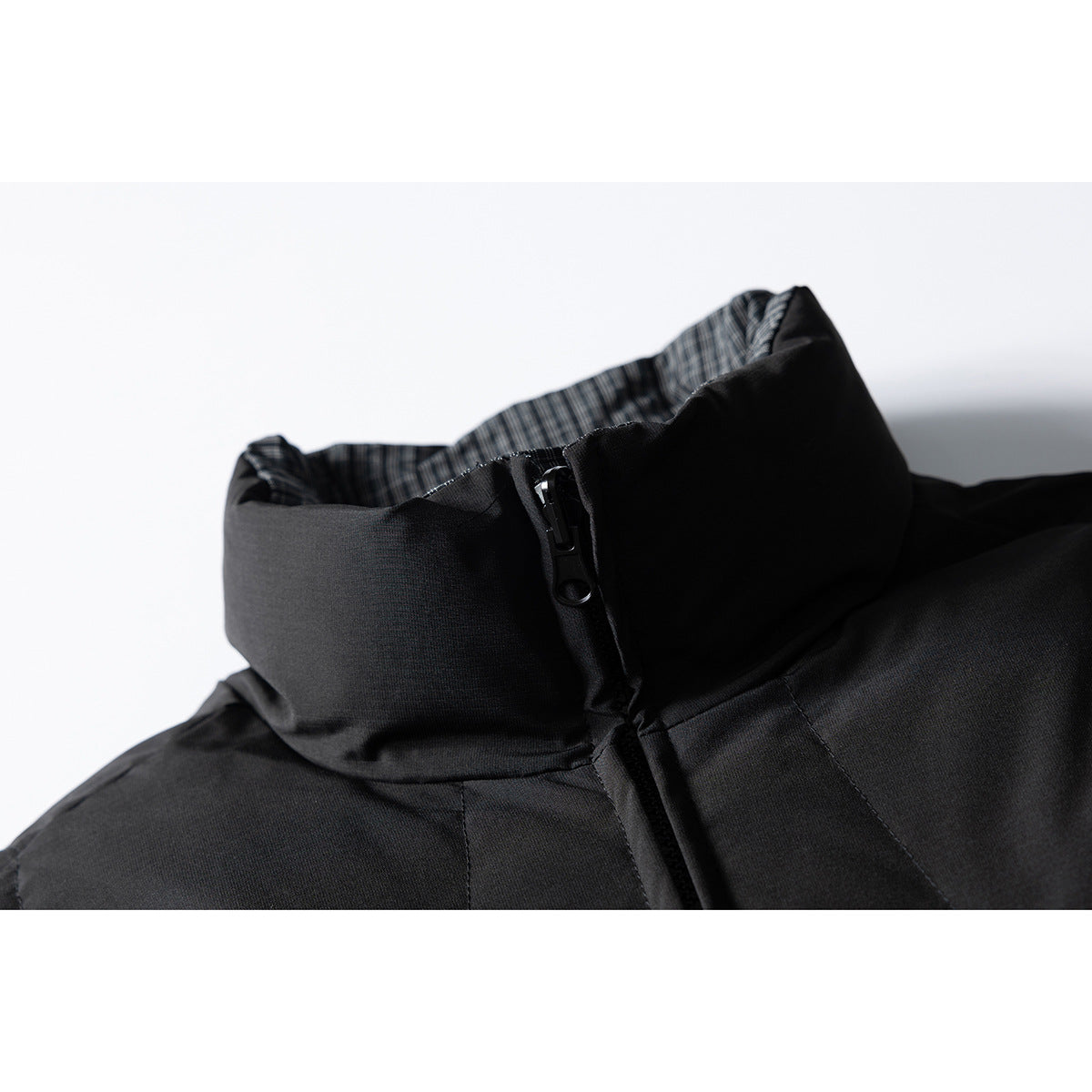 Close-up of a black jacket's high collar, front zipper, and checked inner lining.
