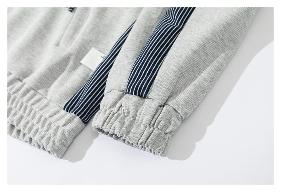 Close-up of light gray joggers showing elastic ankle cuffs and navy-and-white striped side panels.