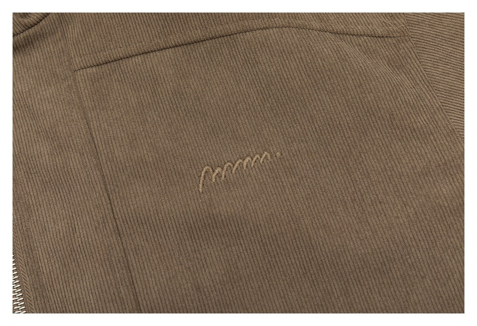 Close-up of taupe ribbed fabric with a small tonal embroidered mark and a seam.