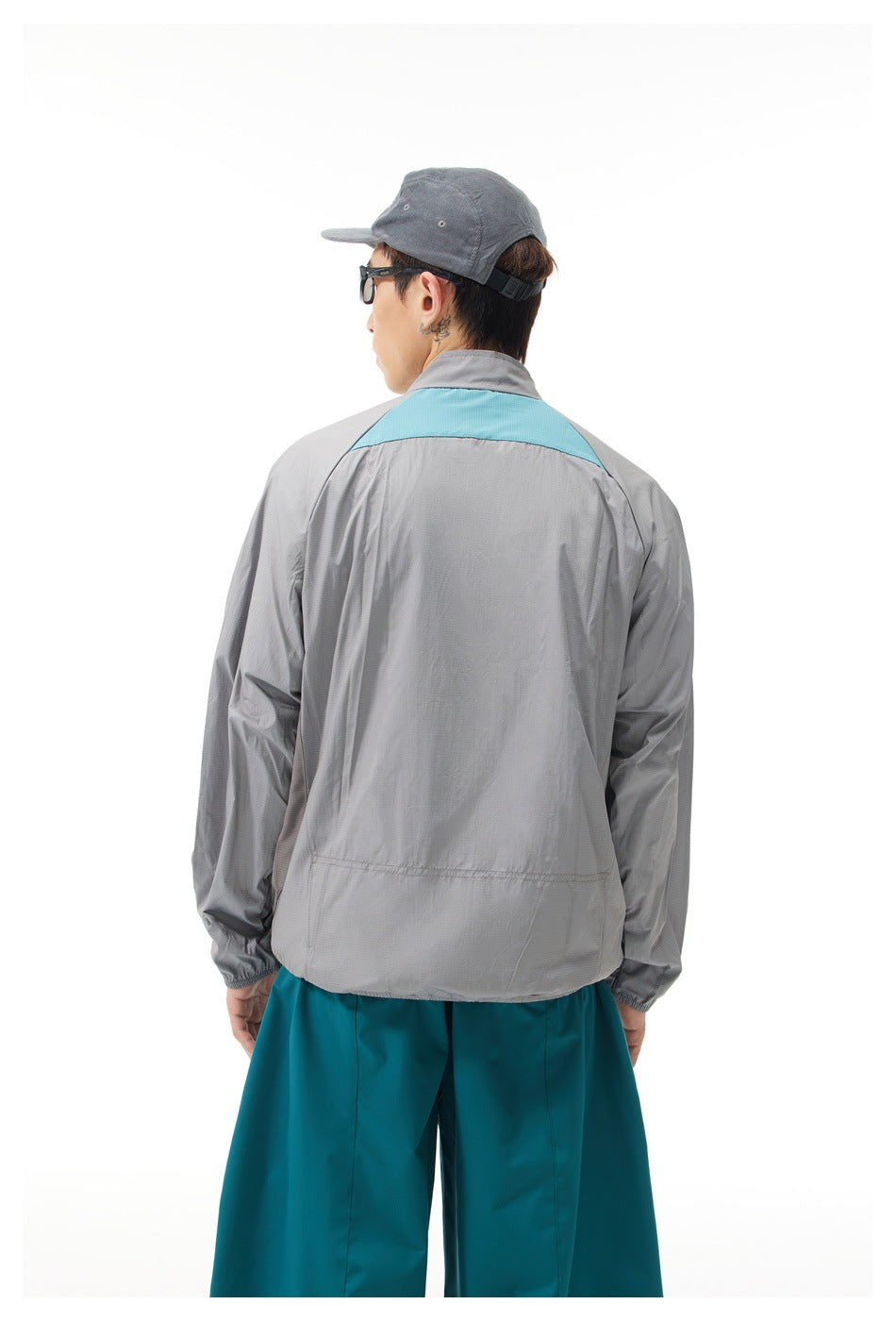 Rear view of a light gray jacket with a turquoise upper-back panel, worn with teal trousers.
