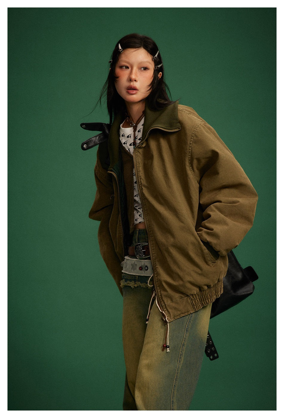 Model in an olive-brown oversized jacket with a dark green ribbed collar and front zip, styled with loose jeans.
