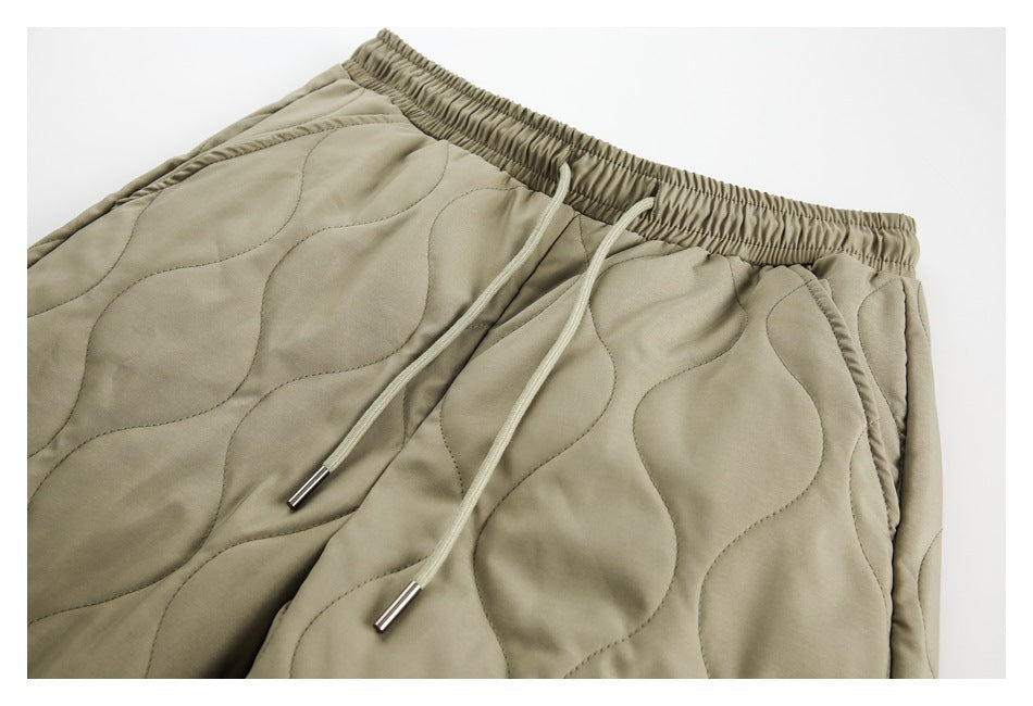 Close-up of olive quilted pants showing the elastic waistband, drawstrings, and side pocket.