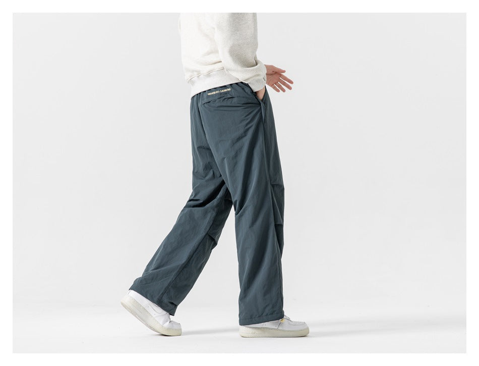 Cropped model wearing loose slate blue-gray pants, shown from the side and rear with white sneakers.