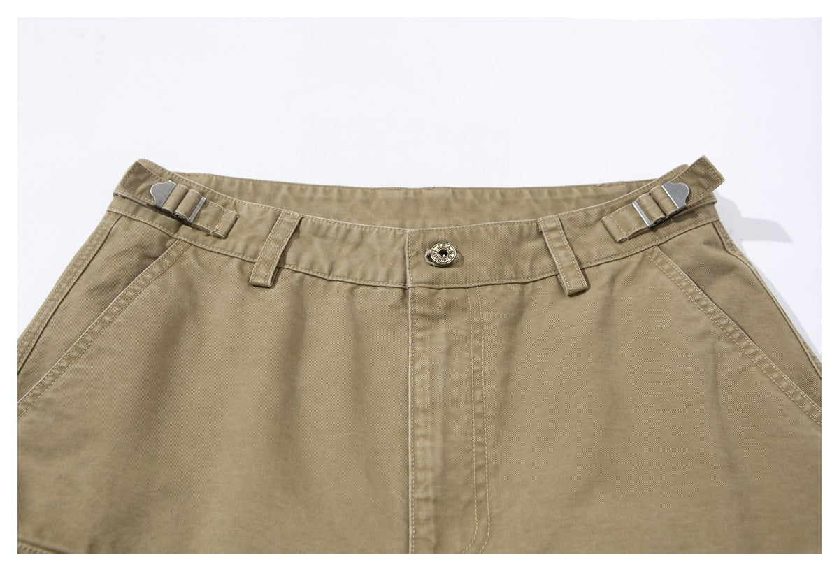 Close-up of khaki trousers showing the waistband, metal side adjusters, belt loops, button, and front fly.