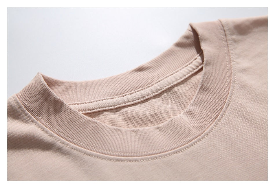 Close-up of the ribbed crew neckline and stitching on a pale blush-pink T-shirt.