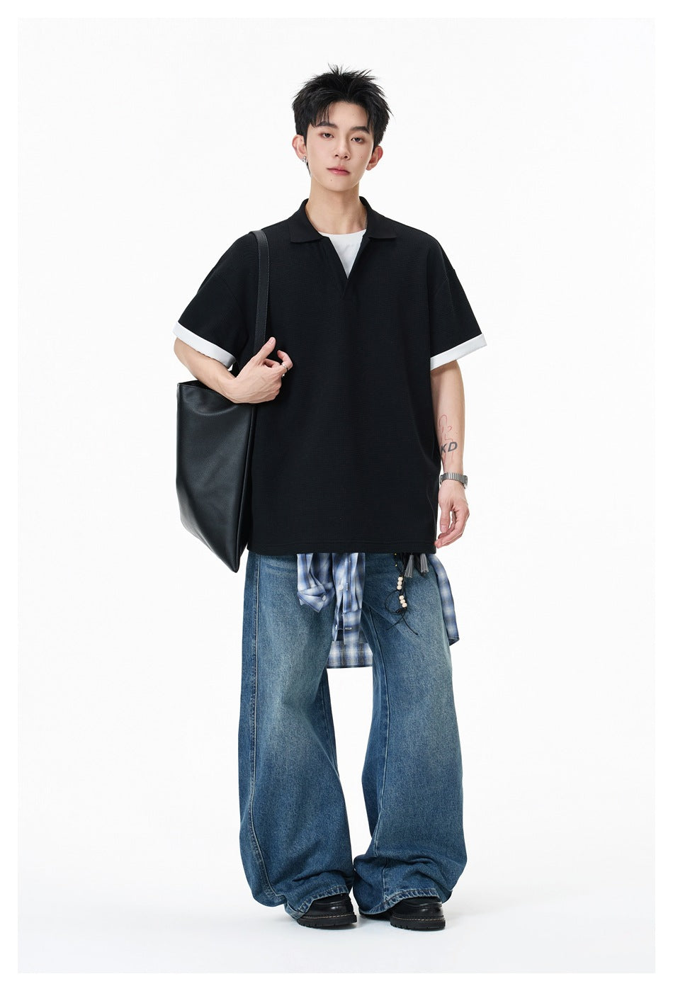 Model wearing black polo-style top with white cuffs, wide-leg jeans and black tote bag, full-length view