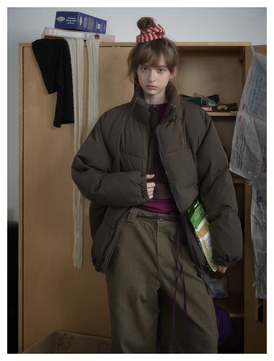 Model wearing an open dark olive-brown puffer jacket with a high collar and roomy sleeves.
